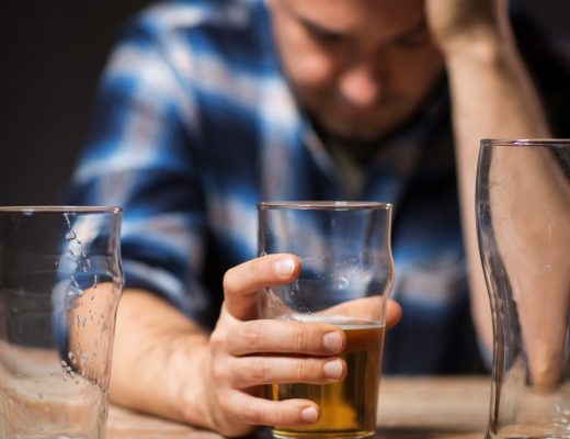 Man hunched over a bar with his hand around an almost-empty beer and two empty beer glasses to his left and right