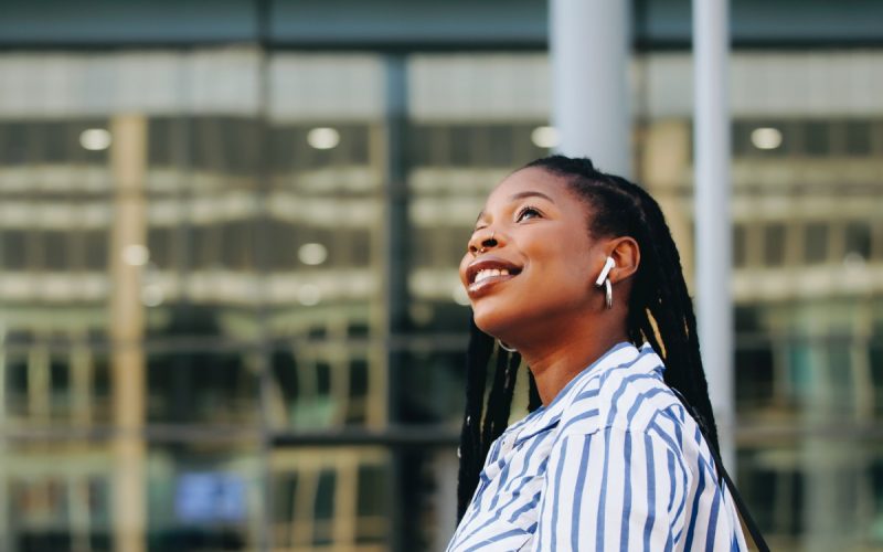 A young professional commuting through her vibrant college town while smiling and texting on her phone.