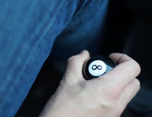 A close-up of someone's hand gripping a decorative eight ball gear shift knob inside a car while driving.