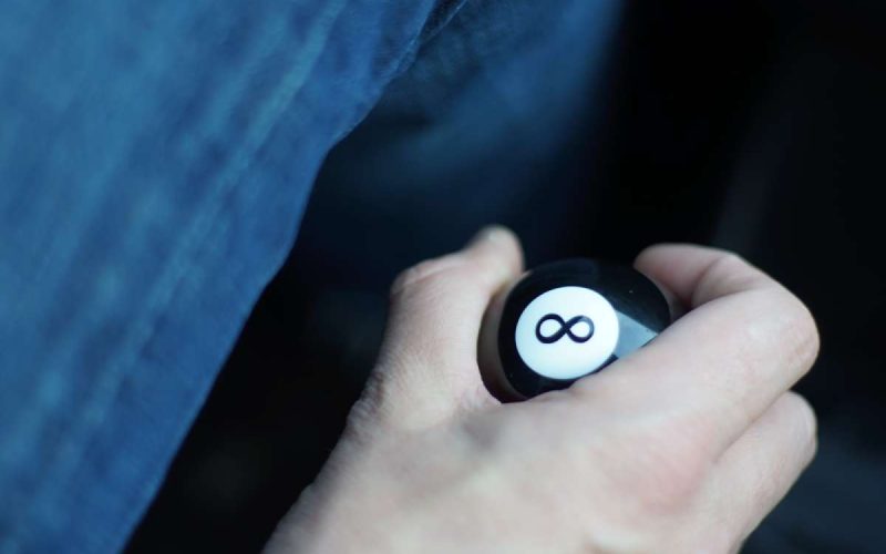 A close-up of someone's hand gripping a decorative eight ball gear shift knob inside a car while driving.