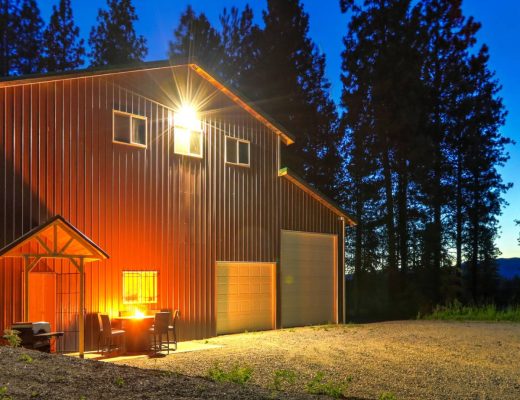 The exterior of a large metal barn with two garage doors. There is a fire pit and outdoor furniture in front of the building.