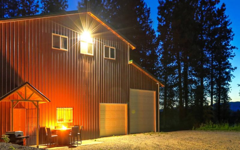 The exterior of a large metal barn with two garage doors. There is a fire pit and outdoor furniture in front of the building.