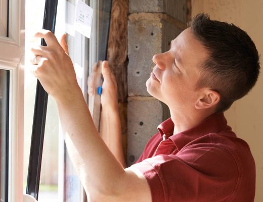 A man carefully installs a replacement window frame, aligning the frame and glass to a partially constructed wall.