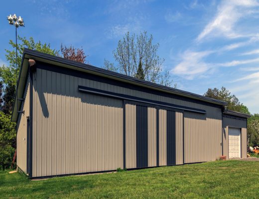 The exterior of a brown and black metal barn on a sunny day. The barn has a flat roof and a white garage door.