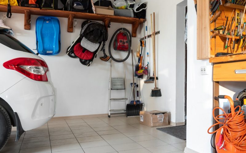 An interior of a garage with the back of a white car on the left and a small workshop desk on the right.