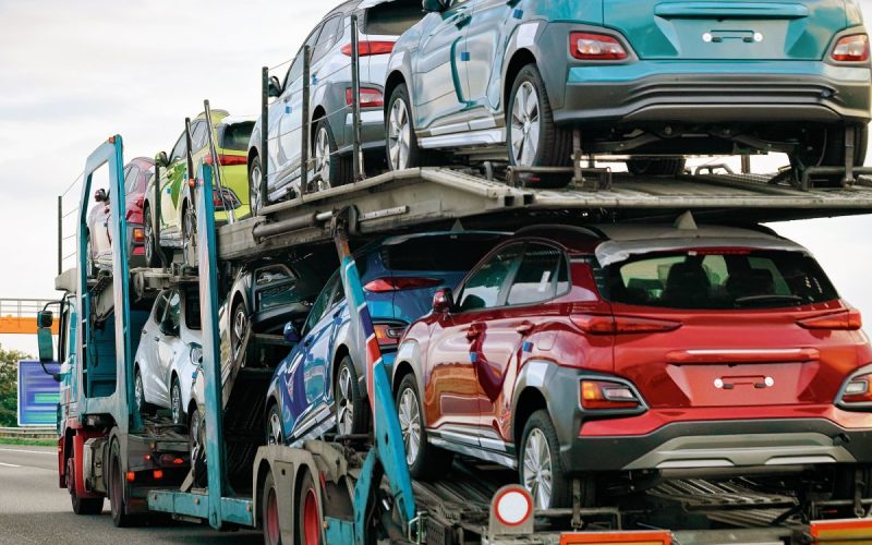 A large truck hauling a trailer with two levels full of cars. The truck is driving on a two-lane highway.