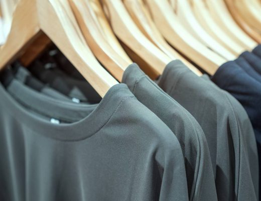 Three gray T-shirts and eight black T-shirts are hanging on wooden hangers on a rack at close range.