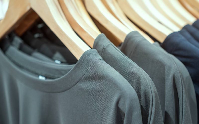 Three gray T-shirts and eight black T-shirts are hanging on wooden hangers on a rack at close range.