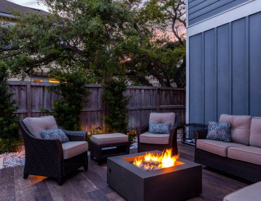 A beautiful, serene outdoor patio space with black furniture and gray cushions. There's a firepit in the center.