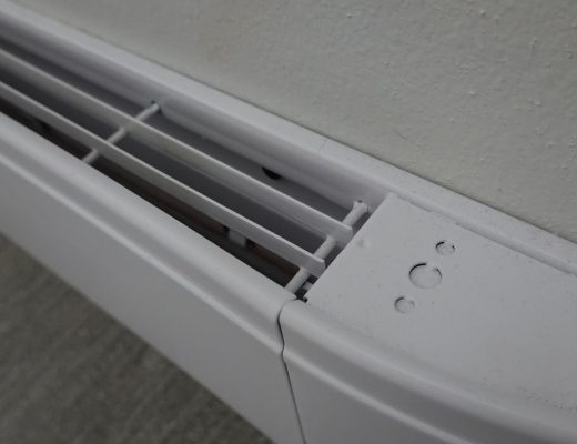 A baseboard heater close up attached to the bottom part of the wall. The wall and heater are both white.