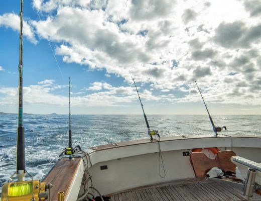 A boat with several large fishing rods mounted on its wooden rail in the open sea on a clear day.