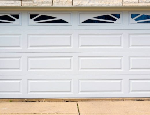 A white sectional garage door with two rounded windows on the top panel on a home with faux stone siding.