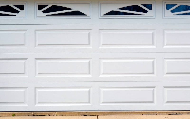 A white sectional garage door with two rounded windows on the top panel on a home with faux stone siding.