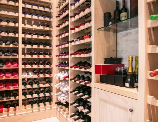 A home wine cellar with bottles placed on their sides in slots. The cellar storage system is wooden with bright lighting.