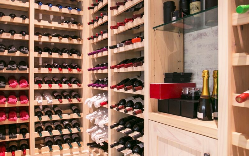 A home wine cellar with bottles placed on their sides in slots. The cellar storage system is wooden with bright lighting.