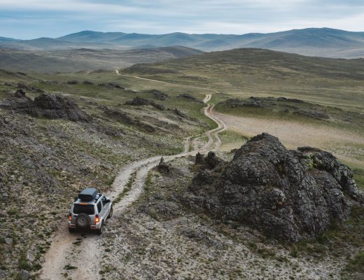A 4x4 SUV drives off-road on rough terrain. The truck is driving through a steppe hills landscape of rocks and stones.