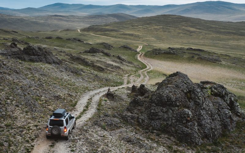 A 4x4 SUV drives off-road on rough terrain. The truck is driving through a steppe hills landscape of rocks and stones.