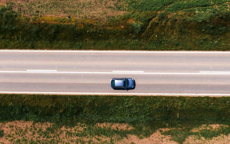 An aerial shot of a car driving along a highway with no trees and shade on a hot sunny summer afternoon.