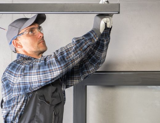 An electrician wearing safety glasses adjusts the support wire on a suspended light fixture during a commercial project.