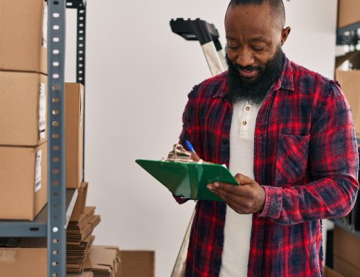 A mature Black man checks off a checklist as he organizes multiple large cardboard boxes in the garage.