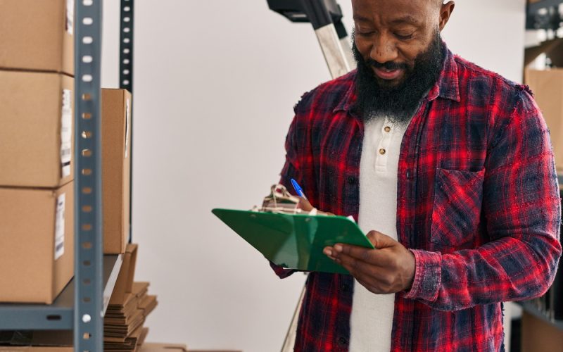 A mature Black man checks off a checklist as he organizes multiple large cardboard boxes in the garage.