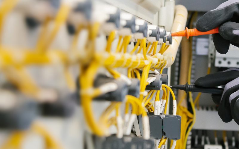 Close-up of an electrical engineer testing electrical wiring on protective relays with a multimeter.