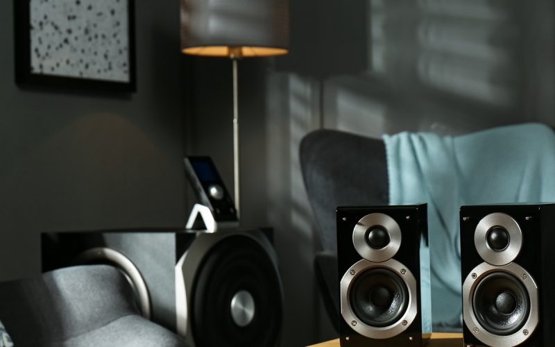 A pair of speakers sit on a wood coffee table. There are two matching gray accent chairs cornering the table.