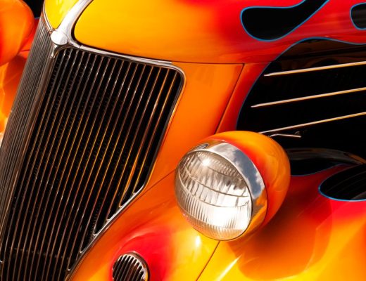 The front of a black hot rod with a large grille, two headlights, and an orange, red, and blue flame decal.