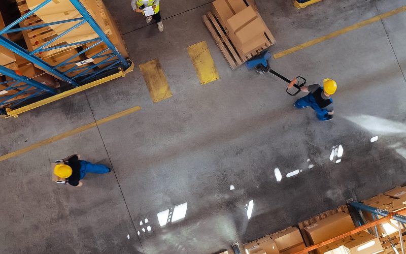 An arial view of a warehouse floor, there are several people around the area. One person is pulling a dolly.