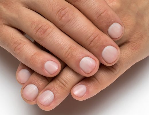 A man's hands show healthy fingernails with a natural pink color and smooth texture against a white background.