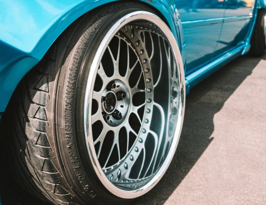 A close-up of the back wheel of a turquoise vehicle that is lowered to the ground. The car's wheels feature unique rims.