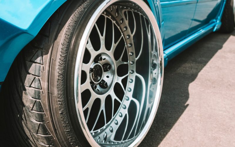 A close-up of the back wheel of a turquoise vehicle that is lowered to the ground. The car's wheels feature unique rims.