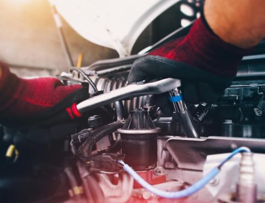 A close-up of a person wearing red and black gloves. They're tightening an auto component with a socket wrench.