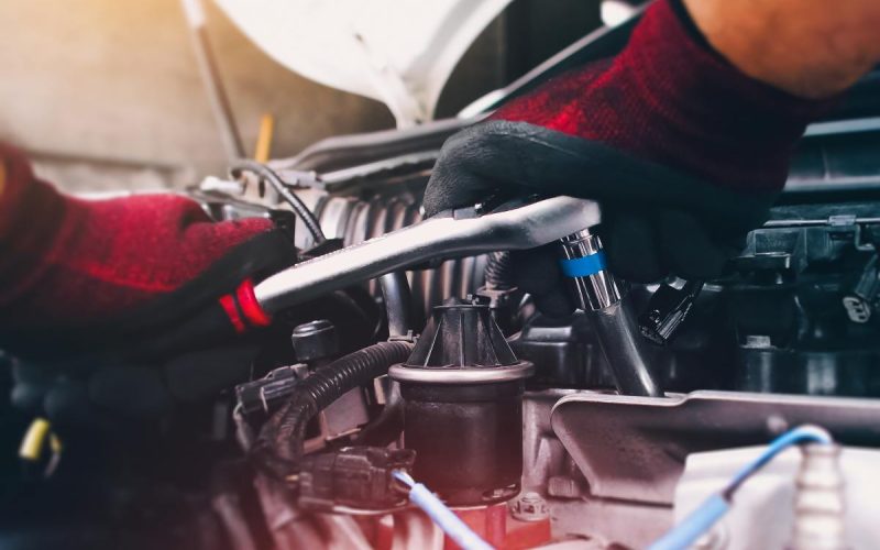 A close-up of a person wearing red and black gloves. They're tightening an auto component with a socket wrench.