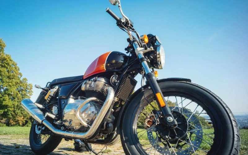 A black and orange motorcycle parked on top of a cobblestone path lined with grass. There are trees in the distance.