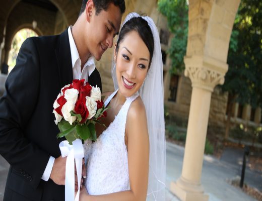 A beautiful bride and groom are excitedly posing and smiling at their wedding venue on their wedding day.