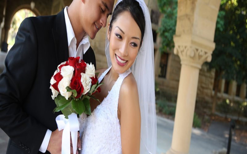 A beautiful bride and groom are excitedly posing and smiling at their wedding venue on their wedding day.
