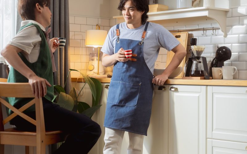 Two young men, both enjoying a drink from a cup, are talking to each other in a kitchen during the day.