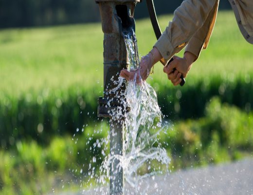 Someone is using the water from the well to wash their hands. They're letting the water run on their hands.