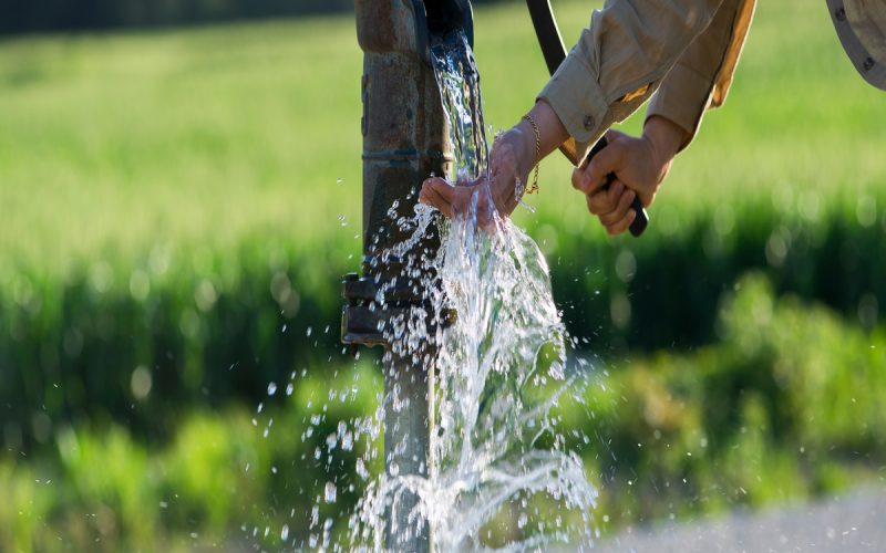 Someone is using the water from the well to wash their hands. They're letting the water run on their hands.