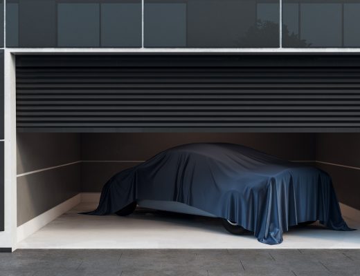 A modern, black and white garage with security cams is half-open, showing a vehicle covered with a black cloth.