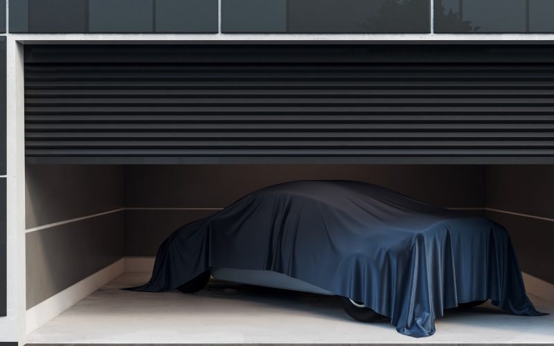 A modern, black and white garage with security cams is half-open, showing a vehicle covered with a black cloth.