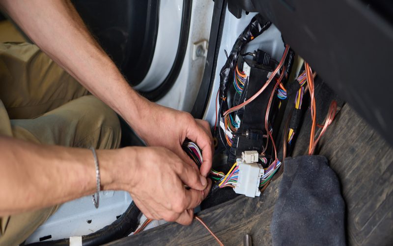 A person using their bare hands to repair wiring in a car. The wires are located on the driver’s side of the vehicle.