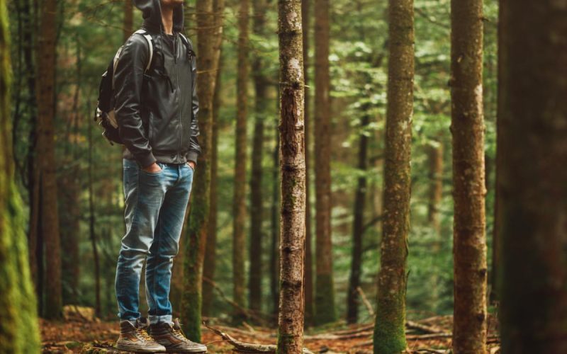 A calm man in hiking gear taking a deep breath while standing on a tree stump in the middle of a green wooded area.
