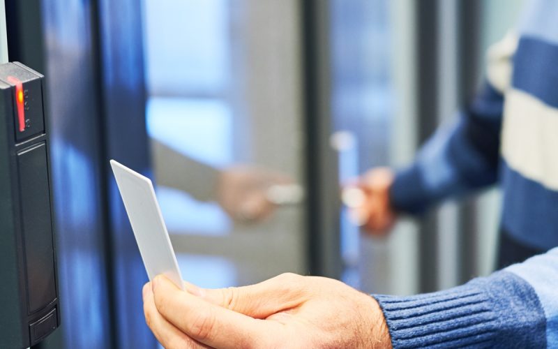 A person wearing a striped blue and white sweater is holding a white key card up to a black card reader.