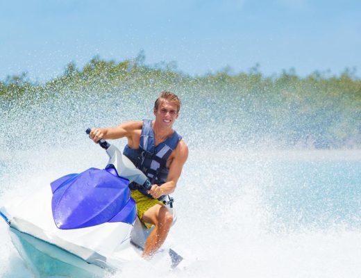 Man riding a jet ski on the water, wearing sunglasses and a life jacket, with small waves splashing around him.