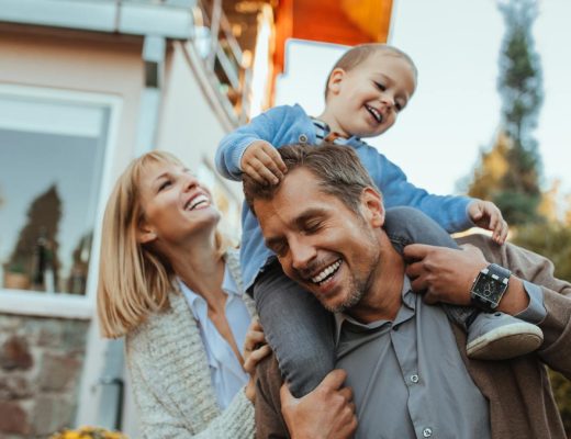 A man is carrying a child on his shoulders as a woman is walking next to him in an outdoor environment.