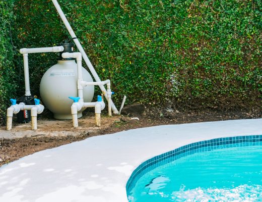 A pool equipment setup, including a filter, pump, and various pipes, on a concrete pad next to a swimming pool.