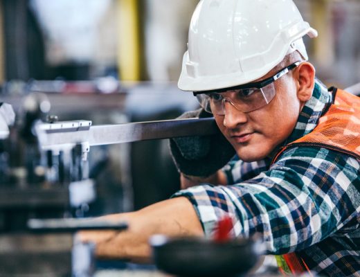 A man wearing a hard hat operating a lathe machine in a workshop with metal equipment and tools around him