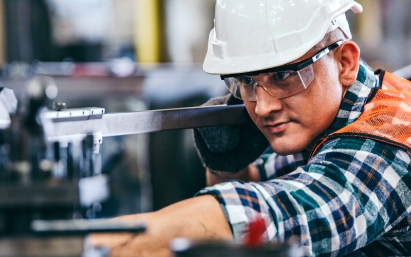 A man wearing a hard hat operating a lathe machine in a workshop with metal equipment and tools around him